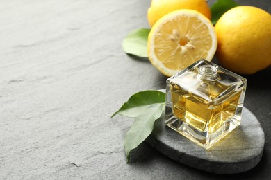 Photo of Open perfume bottle with aromatic essential oil, leaves and lemons on dark textured table, closeup. Space for text
