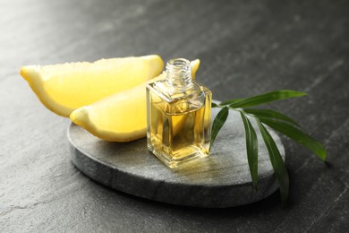 Photo of Open perfume bottle with aromatic essential oil, leaves and slices of lemon on dark textured table, closeup
