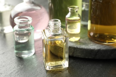 Photo of Open perfume bottles with aromatic essential oils on dark textured table, closeup