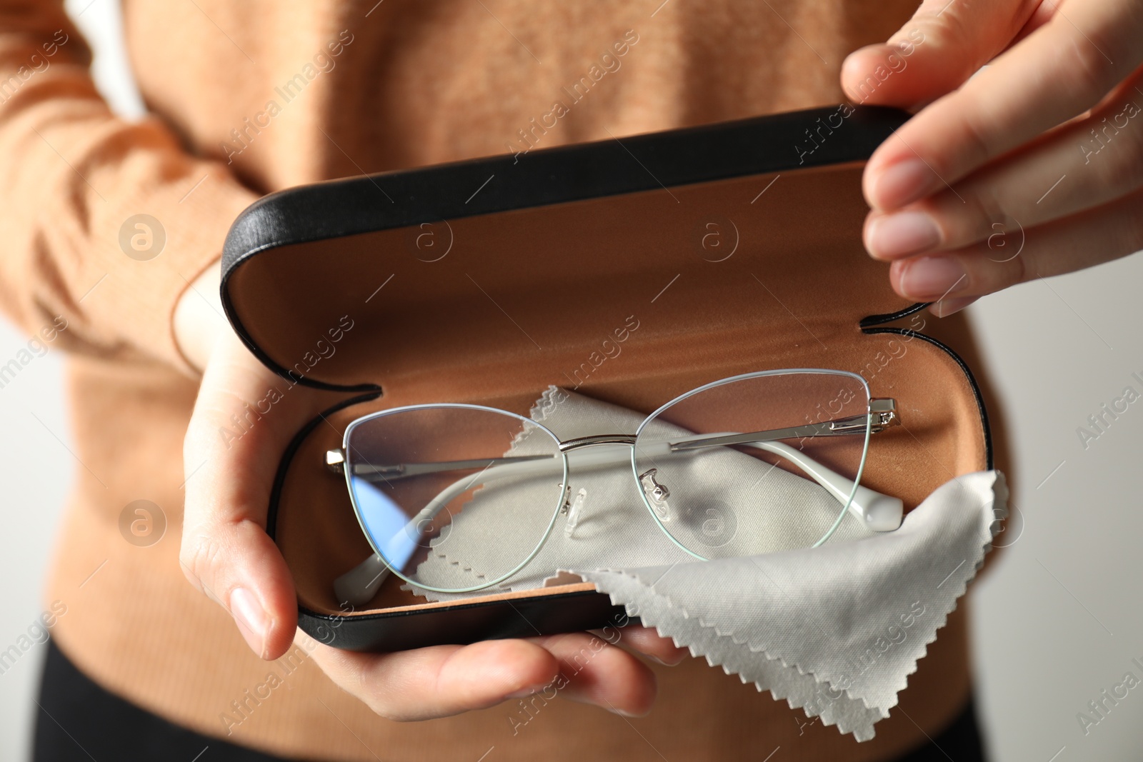 Woman holding case with stylish glasses and cleaning cloth on light background, closeup Photo of Woman holding case with stylish glasses and cleaning cloth on light background, closeup