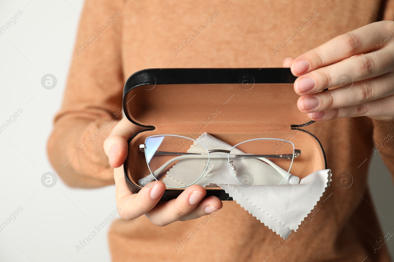 Woman holding case with stylish glasses and cleaning cloth on light background, closeup Photo of Woman holding case with stylish glasses and cleaning cloth on light background, closeup