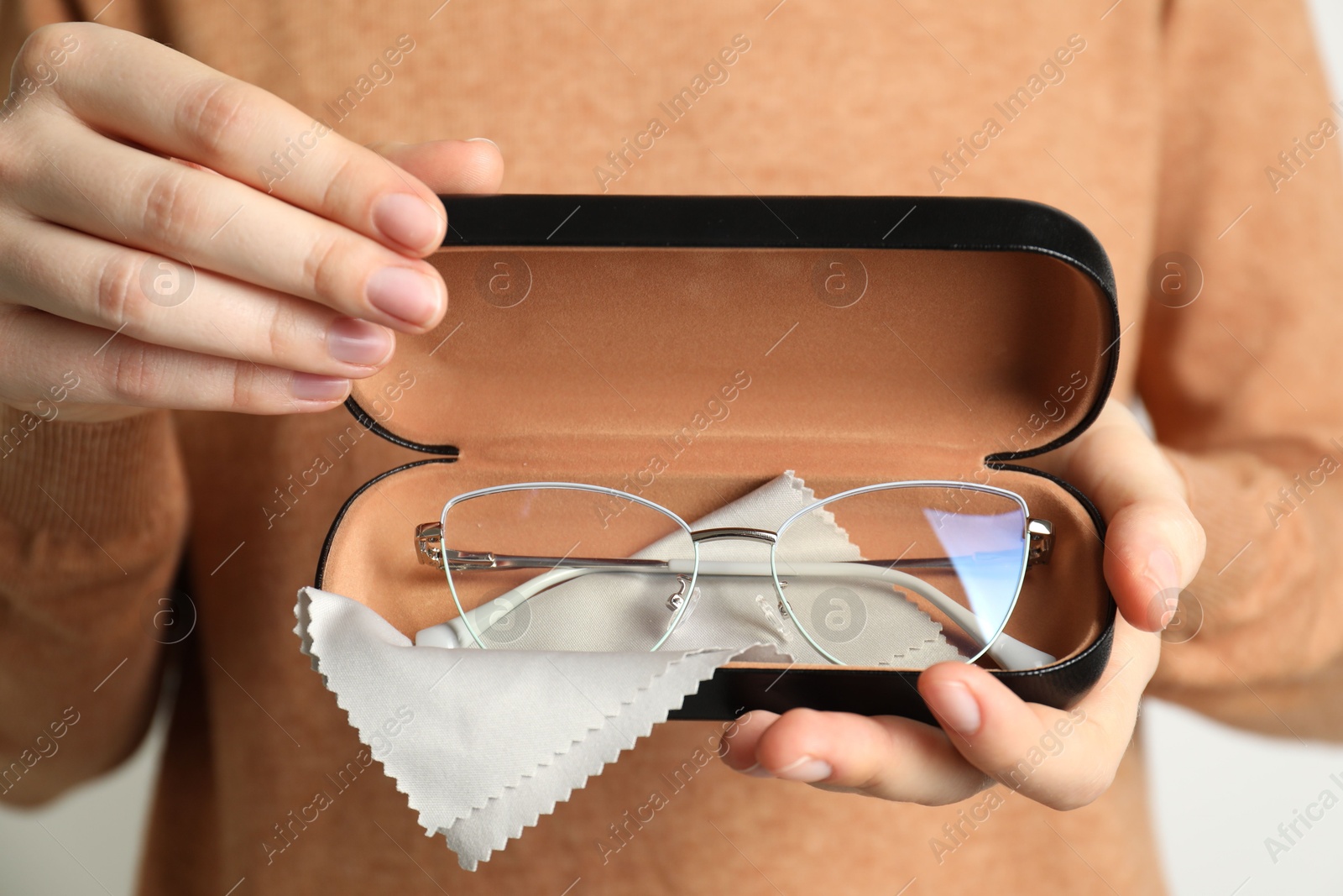 Woman holding case with stylish glasses and cleaning cloth on light background, closeup Photo of Woman holding case with stylish glasses and cleaning cloth on light background, closeup