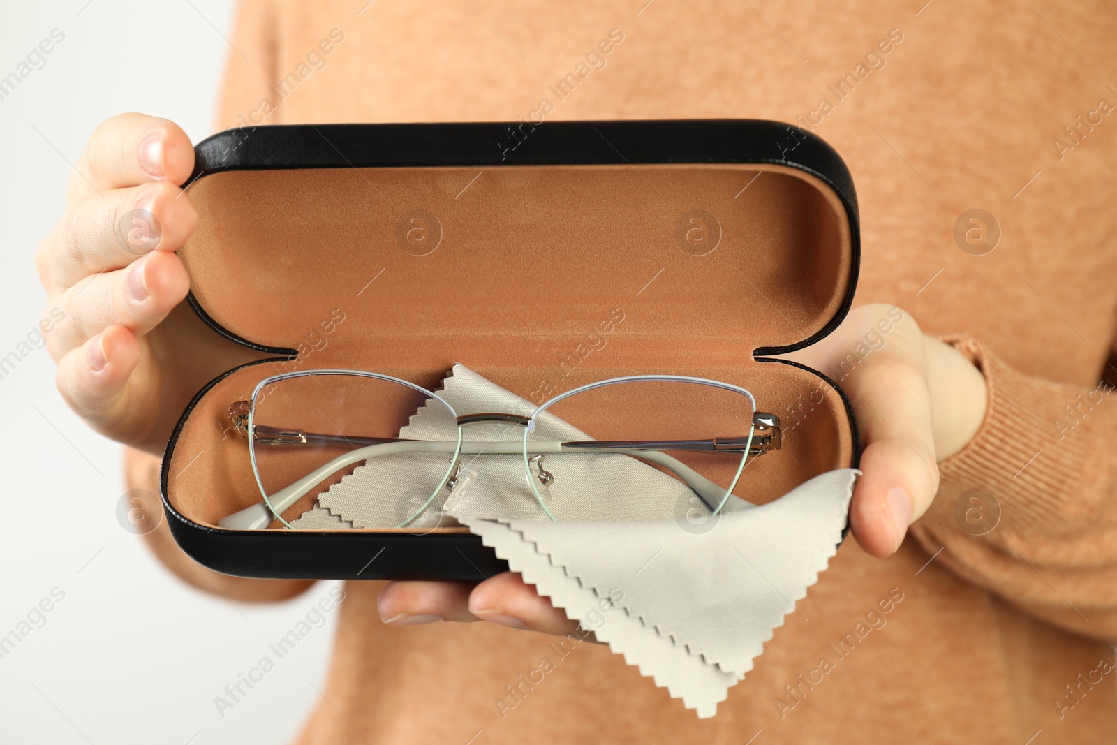 Woman holding case with stylish glasses and cleaning cloth on light background, closeup Photo of Woman holding case with stylish glasses and cleaning cloth on light background, closeup