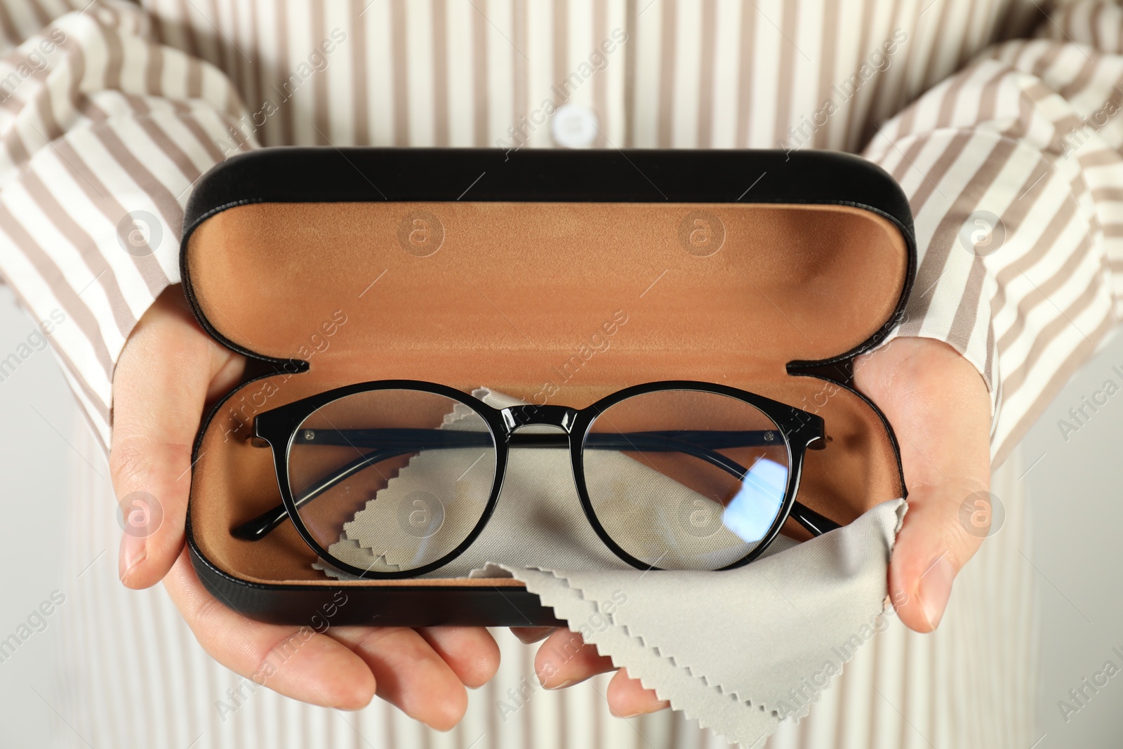 Photo of Woman holding case with stylish glasses and cleaning cloth on light background, closeup