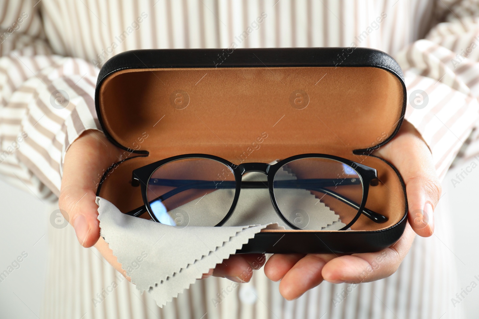 Woman holding case with stylish glasses and cleaning cloth on light background, closeup Photo of Woman holding case with stylish glasses and cleaning cloth on light background, closeup