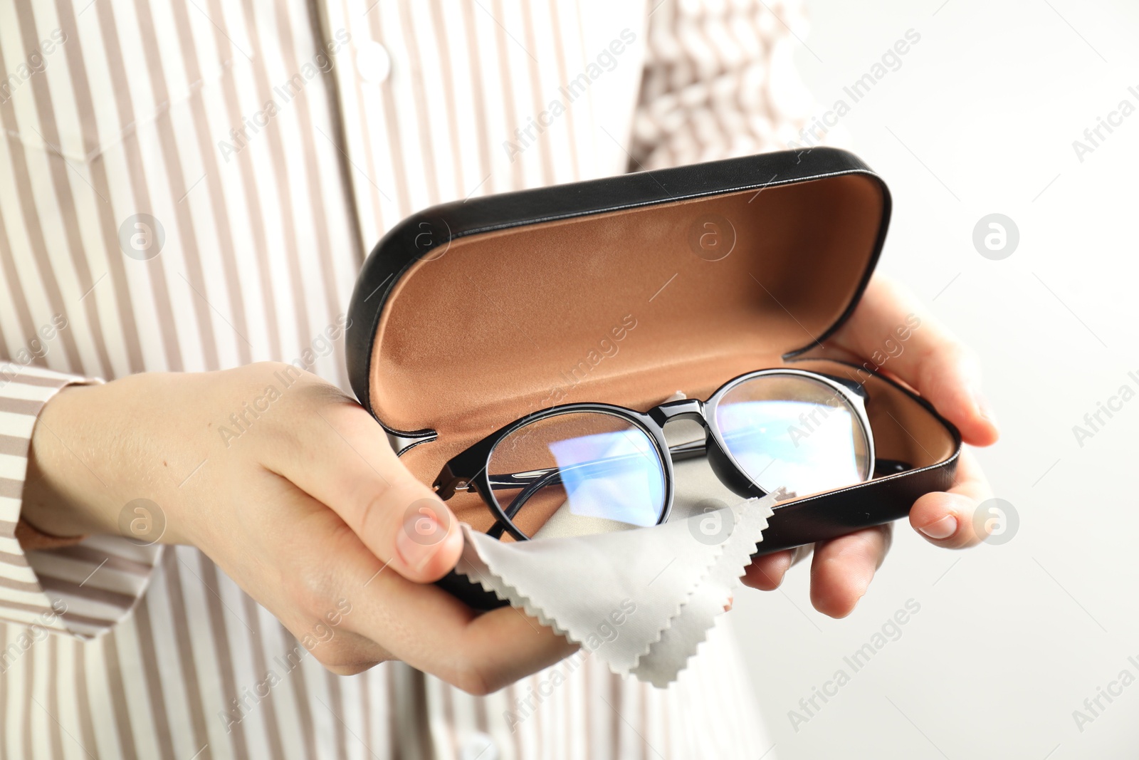 Photo of Woman holding case with stylish glasses and cleaning cloth on light background, closeup