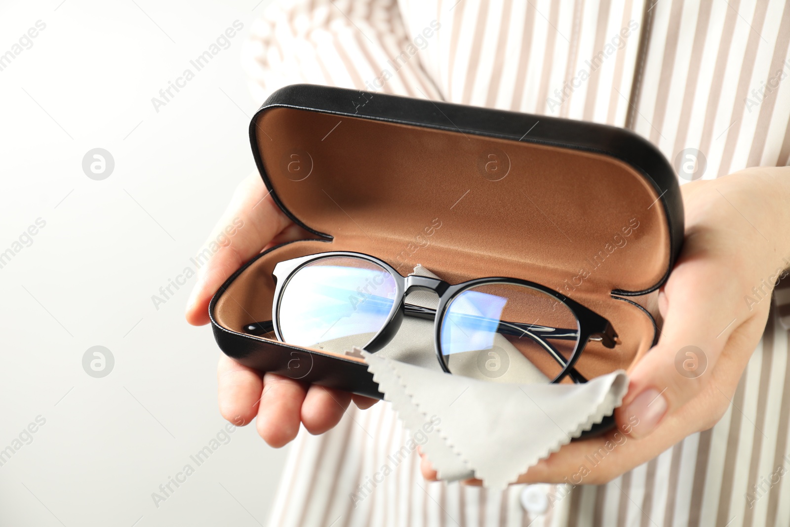Woman holding case with stylish glasses and cleaning cloth on light background, closeup Photo of Woman holding case with stylish glasses and cleaning cloth on light background, closeup
