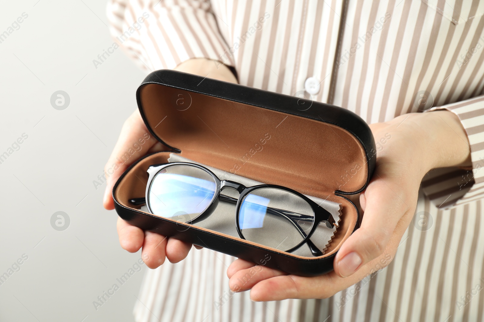 Woman holding case with stylish glasses and cleaning cloth on light background, closeup Photo of Woman holding case with stylish glasses and cleaning cloth on light background, closeup