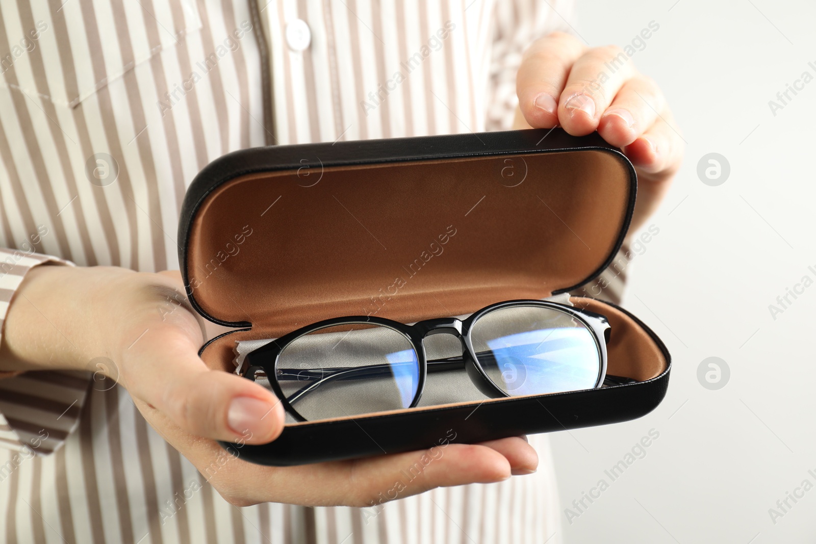 Woman holding case with stylish glasses and cleaning cloth on light background, closeup Photo of Woman holding case with stylish glasses and cleaning cloth on light background, closeup