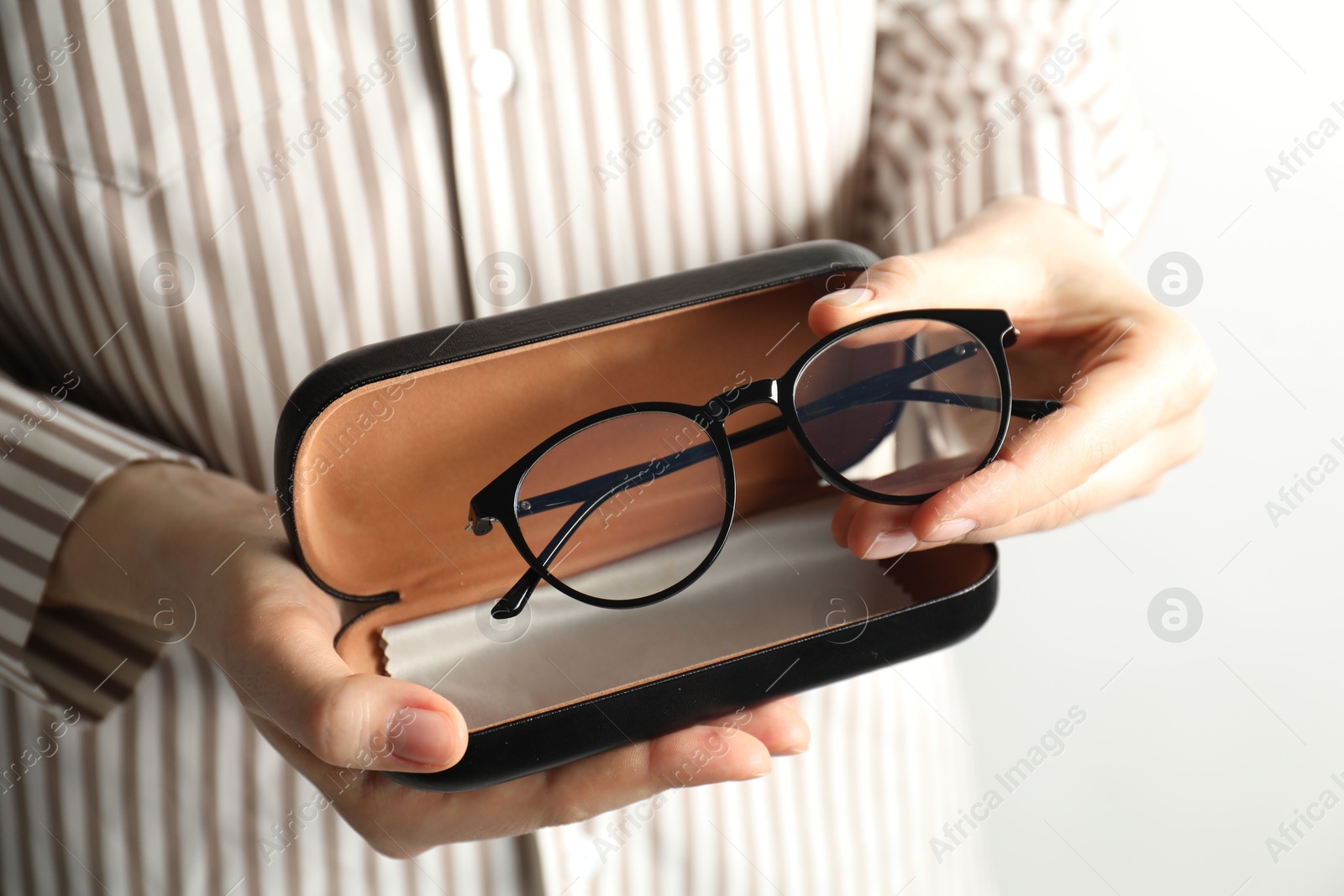 Photo of Woman holding case with stylish glasses and cleaning cloth on light background, closeup