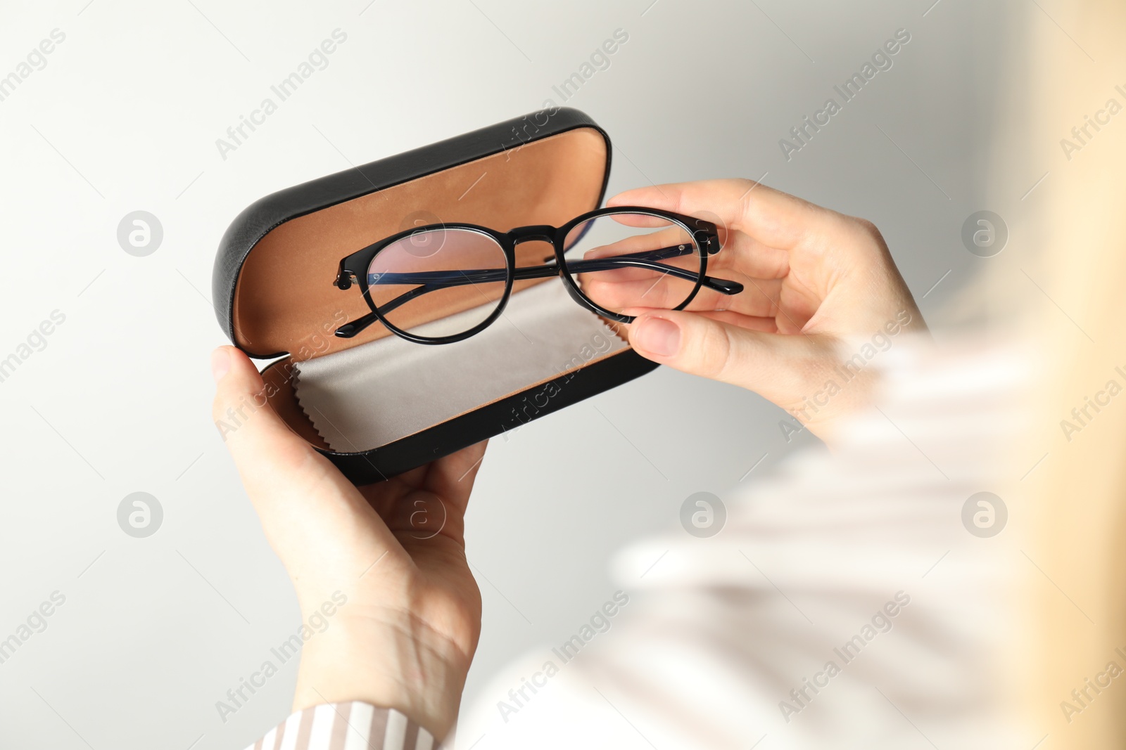 Photo of Woman holding case with stylish glasses and cleaning cloth on light background, closeup