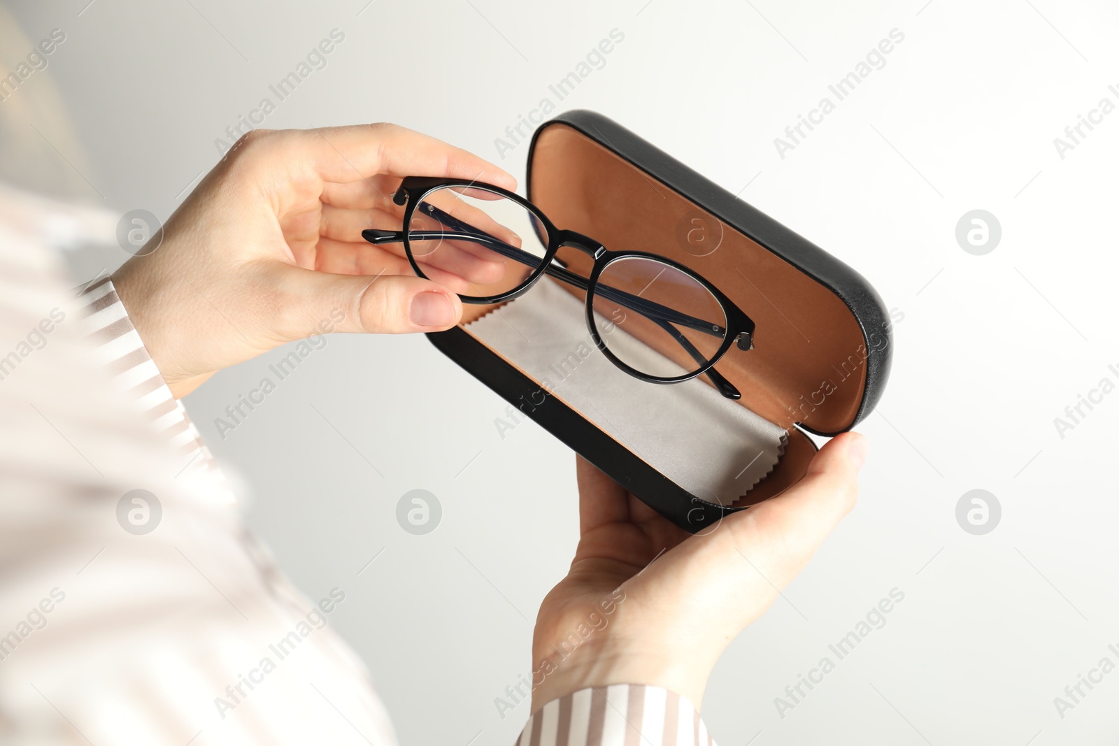 Woman holding case with stylish glasses and cleaning cloth on light background, closeup Photo of Woman holding case with stylish glasses and cleaning cloth on light background, closeup