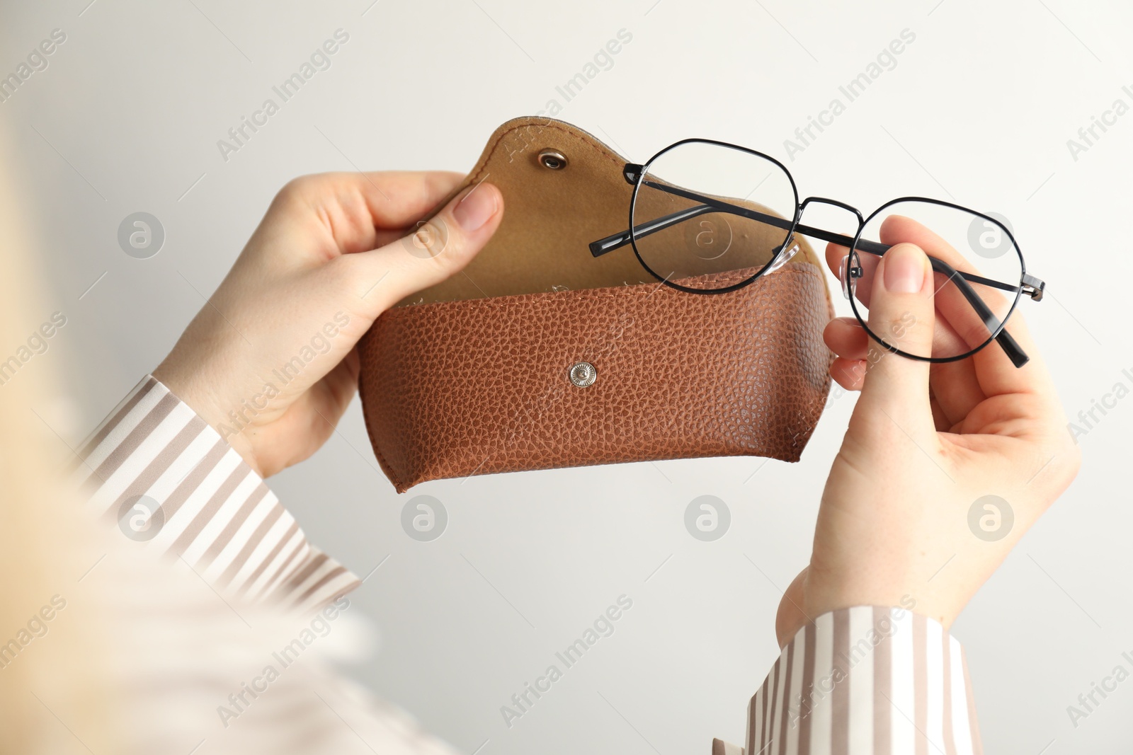 Woman holding case with stylish glasses on light background, closeup Photo of Woman holding case with stylish glasses on light background, closeup
