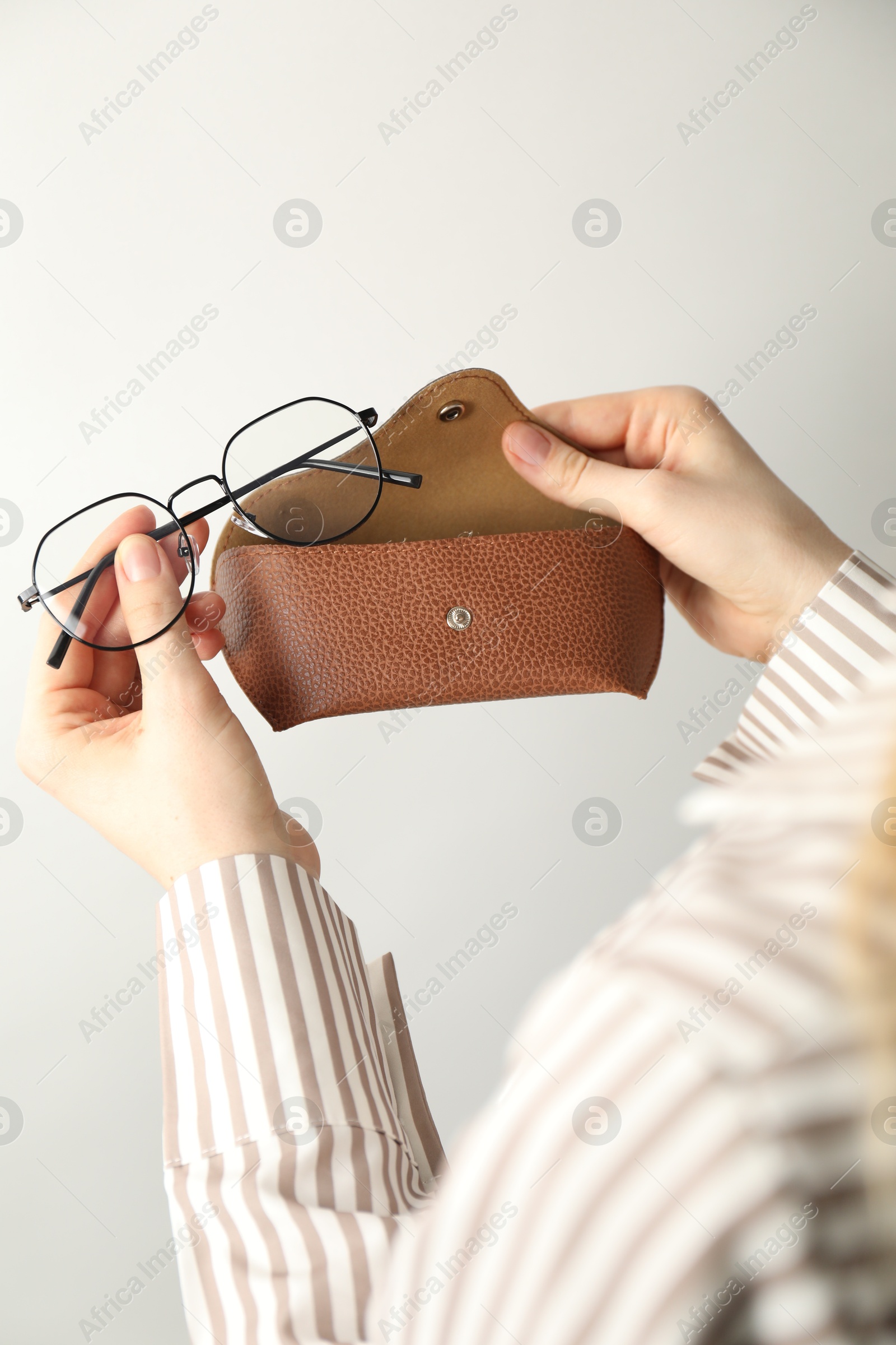 Photo of Woman holding case with stylish glasses on light background, closeup