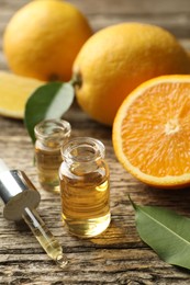 Photo of Open perfume bottles with aromatic essential oils, pipette, oranges and leaves on wooden table, closeup