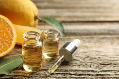 Photo of Open perfume bottles with aromatic essential oils, pipette, oranges and leaves on wooden table, closeup. Space for text