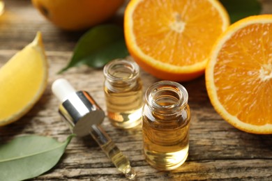 Photo of Open perfume bottles with aromatic essential oils, pipette, oranges and leaves on wooden table, closeup
