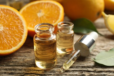 Photo of Open perfume bottles with aromatic essential oils, pipette, oranges and leaves on wooden table, closeup