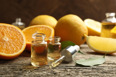 Photo of Open perfume bottles with aromatic essential oils, pipette, oranges and leaves on wooden table, closeup