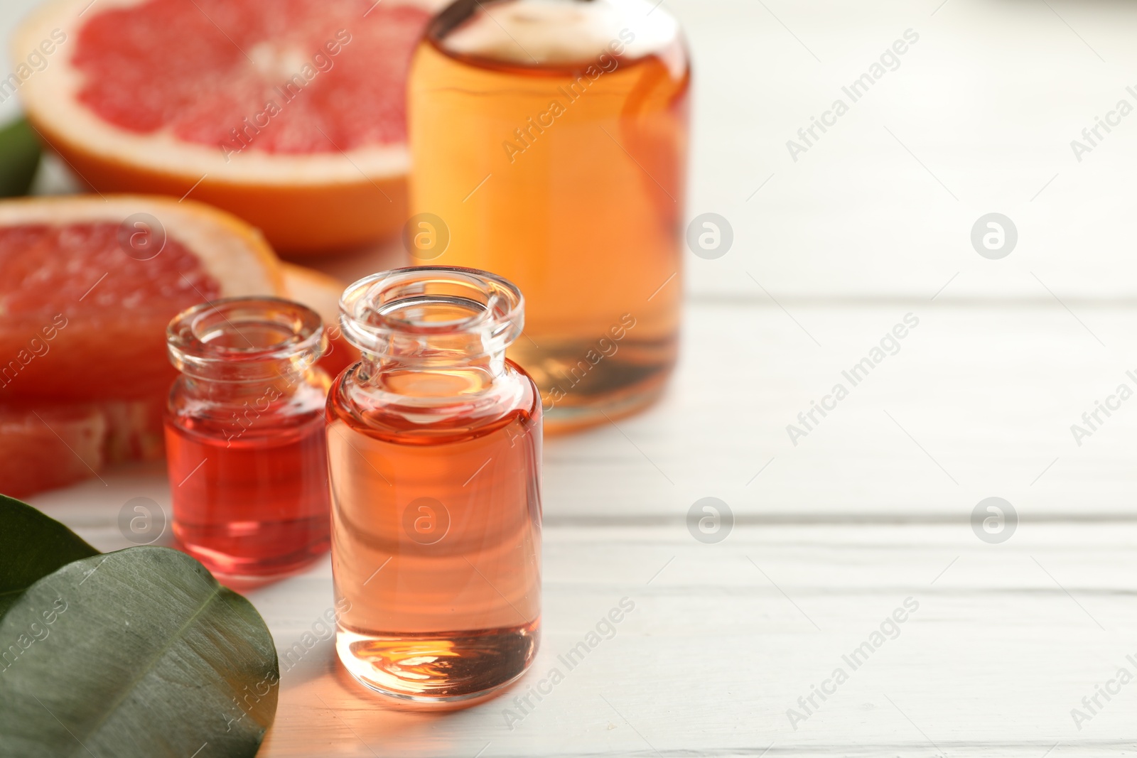 Photo of Open perfume bottles with aromatic essential oils, leaves and slices of grapefruit on white wooden table, closeup. Space for text