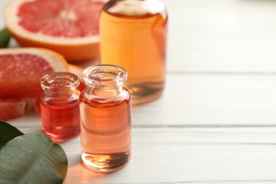Photo of Open perfume bottles with aromatic essential oils, leaves and slices of grapefruit on white wooden table, closeup. Space for text