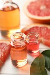 Photo of Open perfume bottles with aromatic essential oils, leaves and slices of grapefruit on white wooden table, closeup