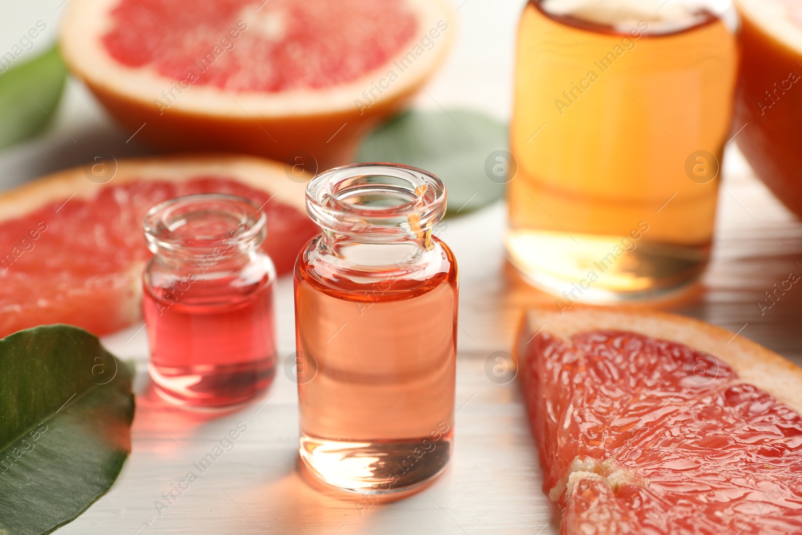 Photo of Open perfume bottles with aromatic essential oils, leaves and slices of grapefruit on white wooden table, closeup