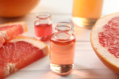 Photo of Open perfume bottles with aromatic essential oils and slices of grapefruit on white wooden table, closeup