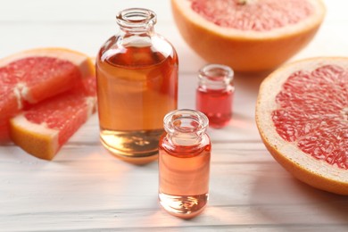 Photo of Open perfume bottles with aromatic essential oils and slices of grapefruit on white wooden table, closeup