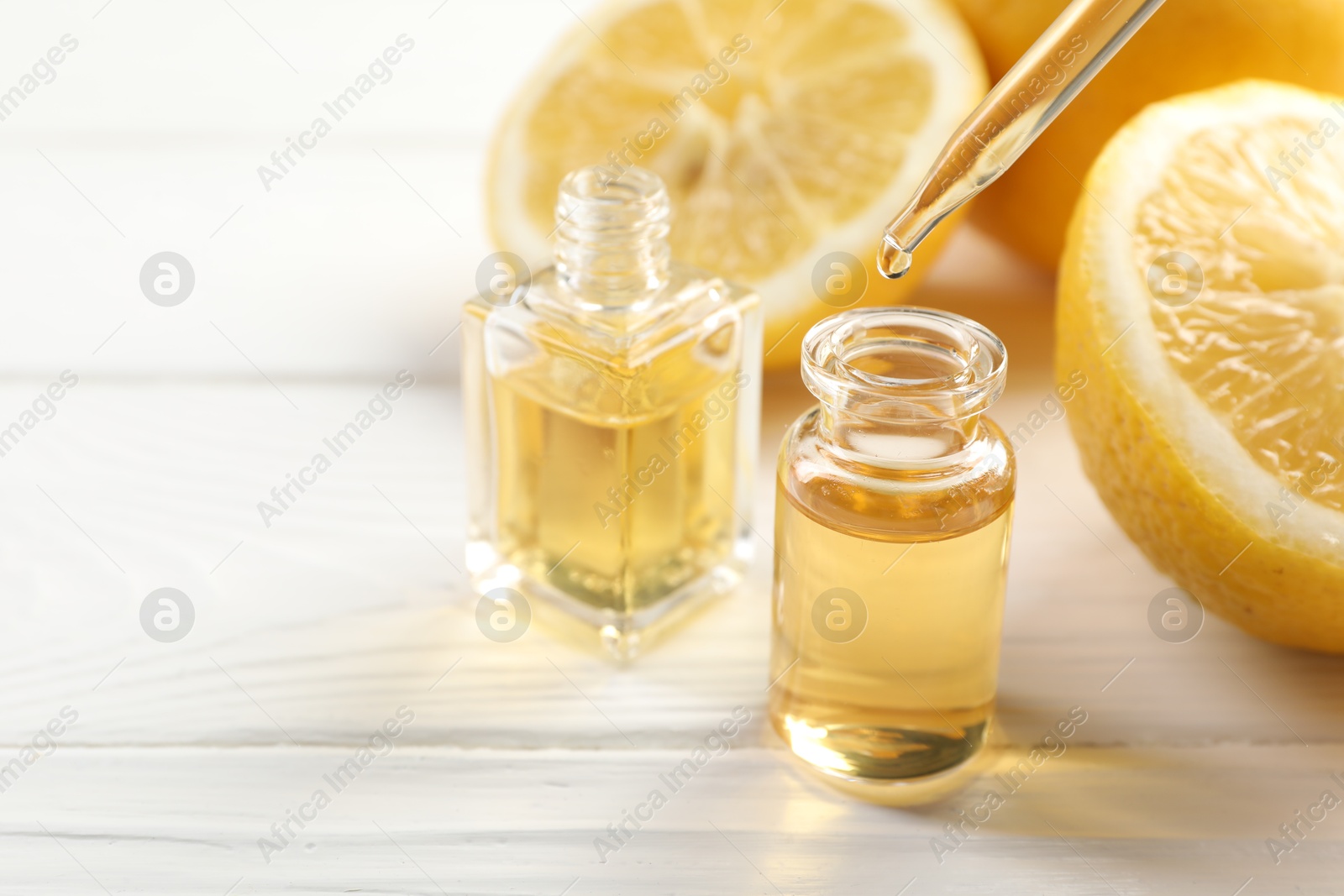 Dripping aromatic essential oil from pipette into perfume bottle and lemons at white wooden table, closeup. Space for text Photo of Dripping aromatic essential oil from pipette into perfume bottle and lemons at white wooden table, closeup. Space for text
