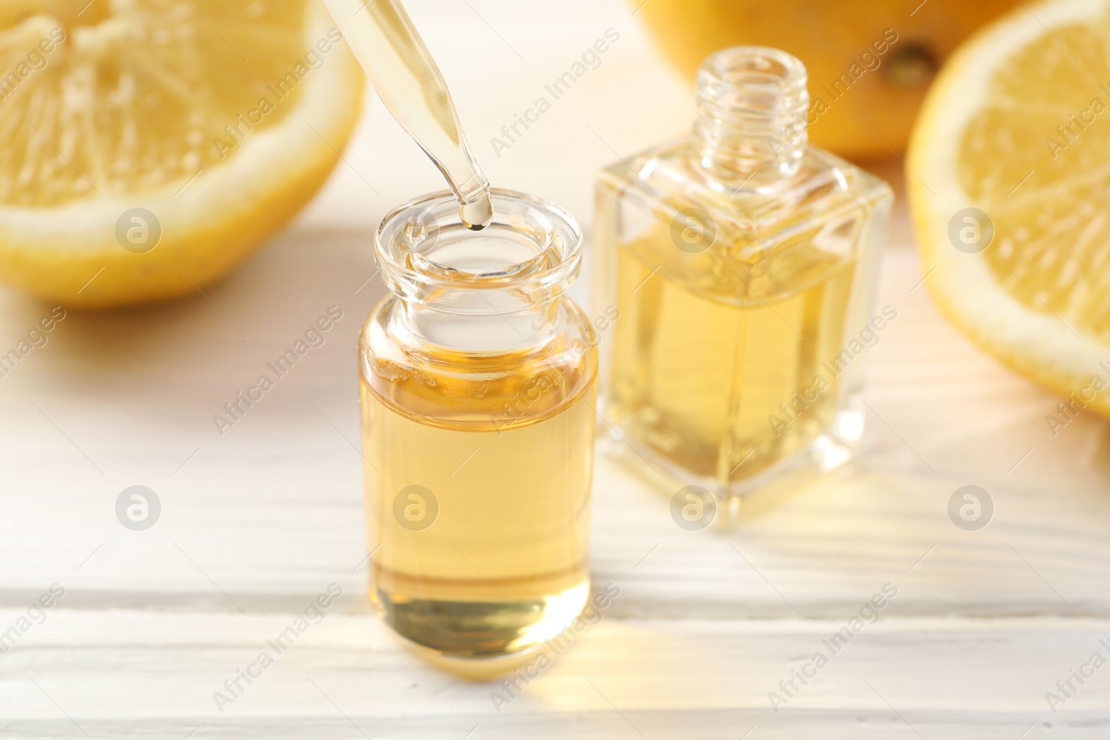 Dripping aromatic essential oil from pipette into perfume bottle and lemons at white wooden table, closeup Photo of Dripping aromatic essential oil from pipette into perfume bottle and lemons at white wooden table, closeup