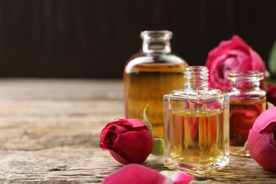 Photo of Open perfume bottles with aromatic essential oils and roses on wooden table, closeup. Space for text