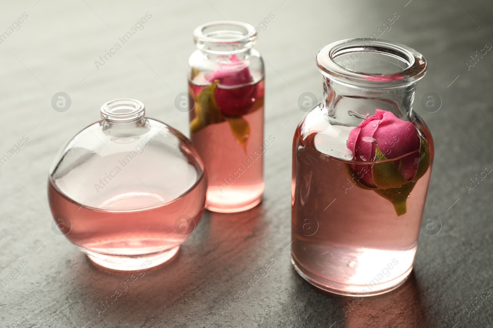 Open perfume bottles with aromatic essential oils and roses on grey textured table, closeup Photo of Open perfume bottles with aromatic essential oils and roses on grey textured table, closeup