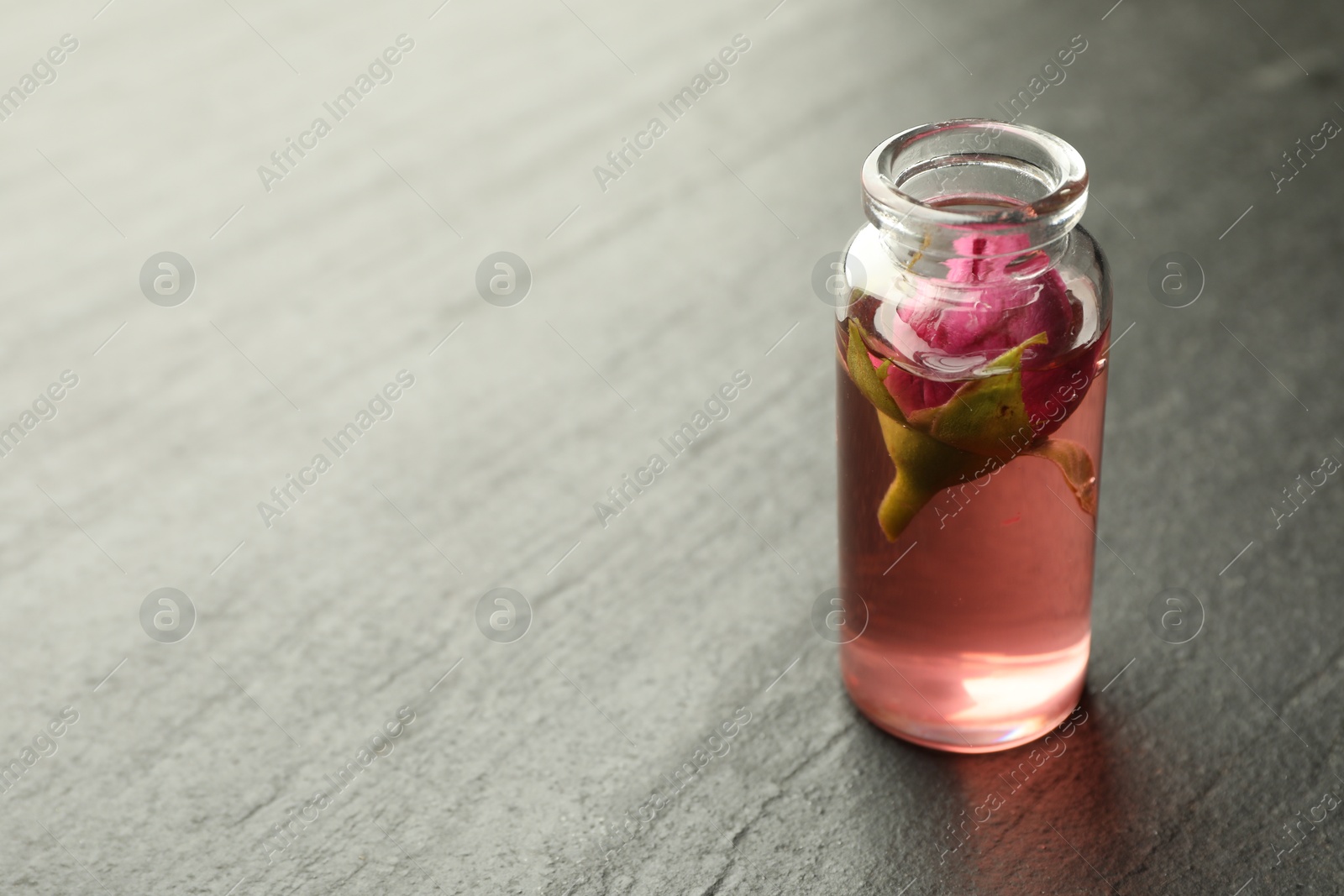 Open perfume bottle with aromatic essential oil and rose on grey textured table, closeup. Space for text Photo of Open perfume bottle with aromatic essential oil and rose on grey textured table, closeup. Space for text