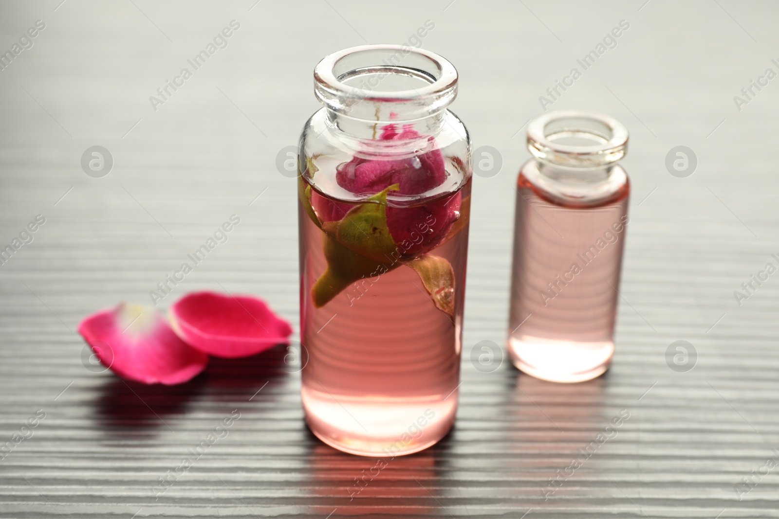 Open perfume bottles with aromatic essential oils and rose petals on grey wooden table, closeup Photo of Open perfume bottles with aromatic essential oils and rose petals on grey wooden table, closeup