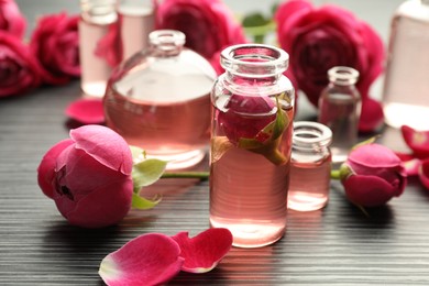 Photo of Open perfume bottles with aromatic essential oils and roses on grey wooden table, closeup