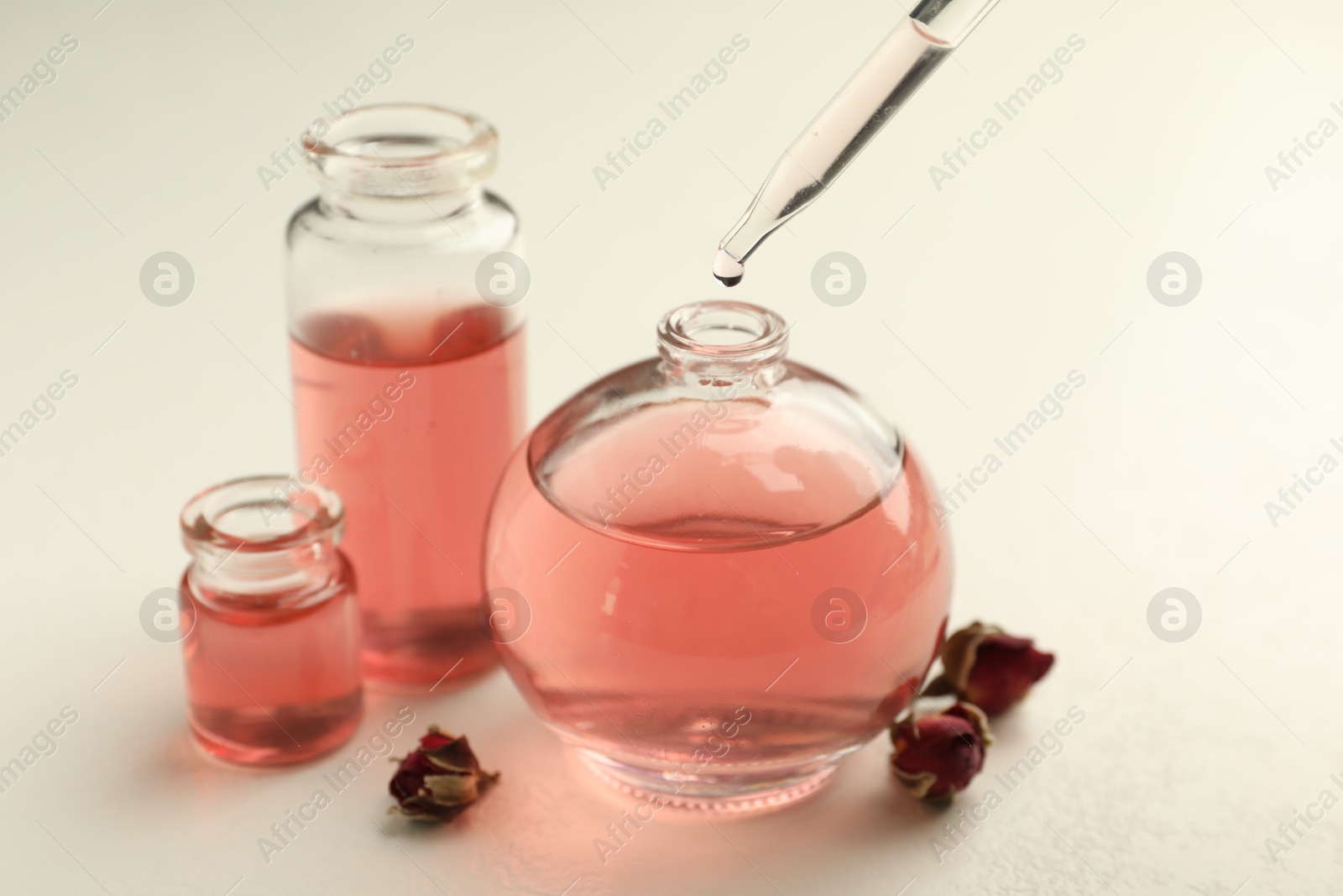 Dripping essential oil into open perfume bottle on white table, closeup Photo of Dripping essential oil into open perfume bottle on white table, closeup