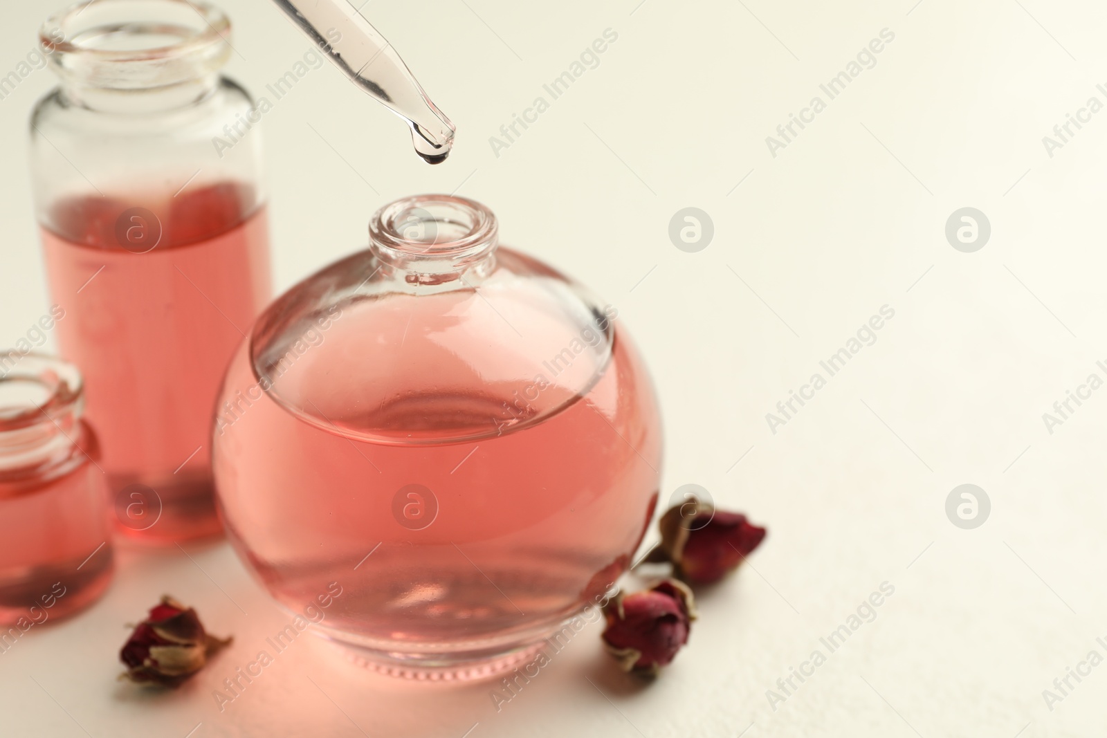 Dripping essential oil into open perfume bottle on white table, closeup Photo of Dripping essential oil into open perfume bottle on white table, closeup