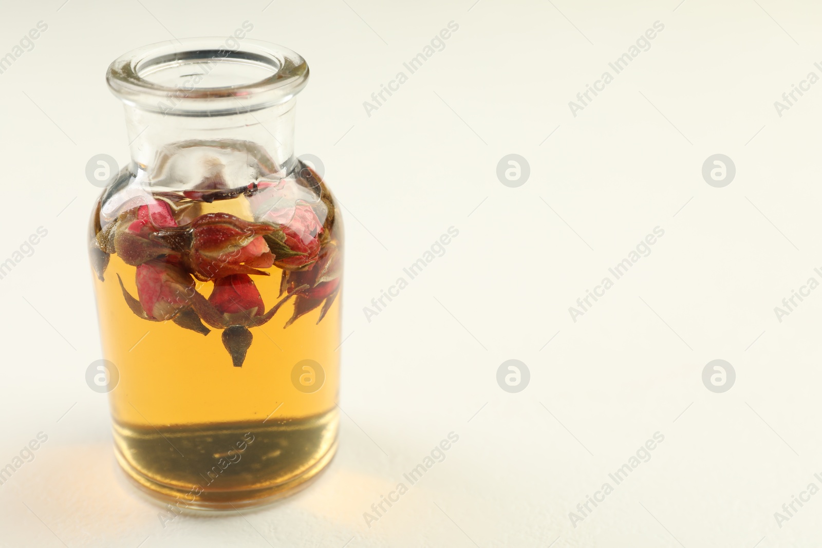 Open perfume bottle with aromatic essential oil and dried roses on white table, closeup. Space for text Photo of Open perfume bottle with aromatic essential oil and dried roses on white table, closeup. Space for text