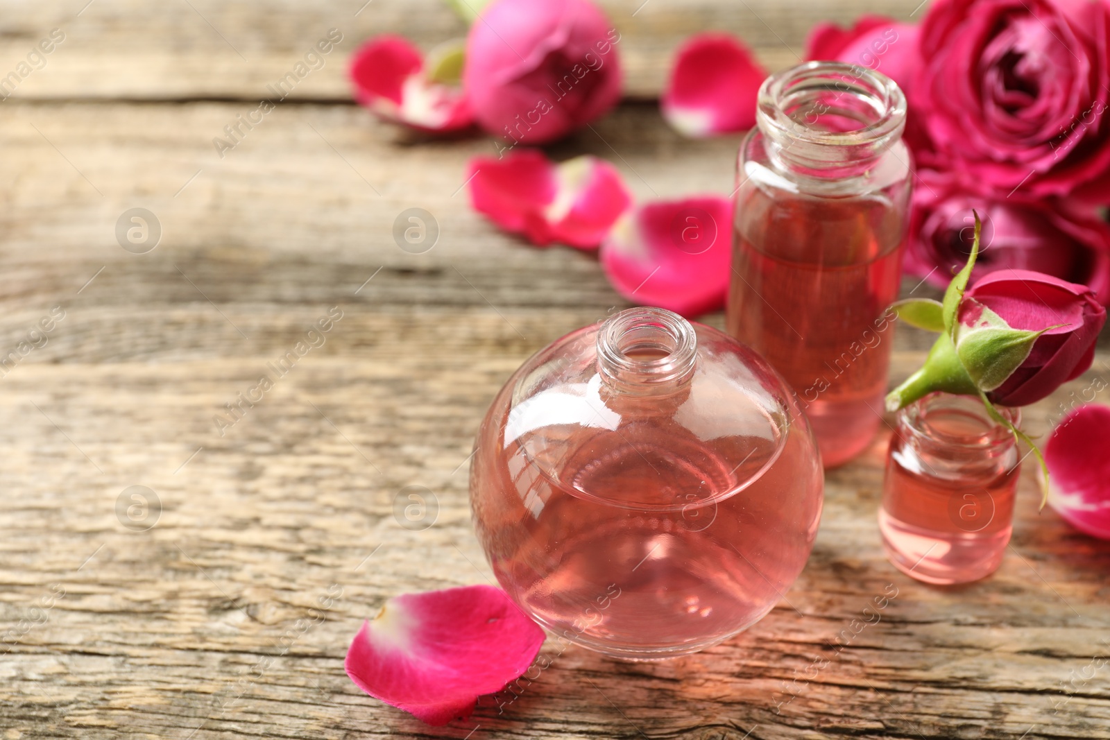 Open perfume bottles with aromatic essential oils and roses on wooden table, closeup. Space for text Photo of Open perfume bottles with aromatic essential oils and roses on wooden table, closeup. Space for text