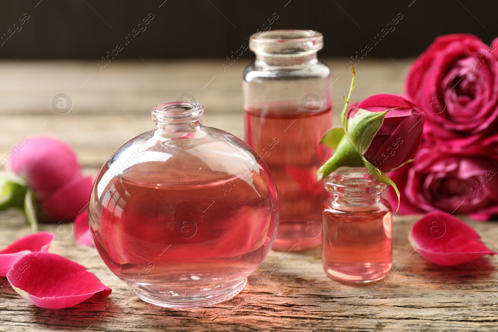 Open perfume bottles with aromatic essential oils and roses on wooden table, closeup Photo of Open perfume bottles with aromatic essential oils and roses on wooden table, closeup