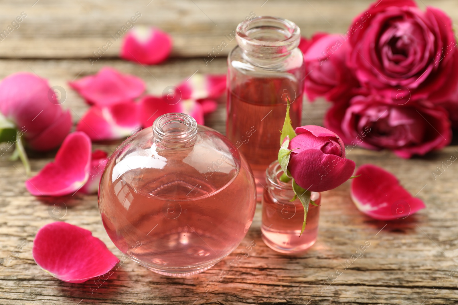 Open perfume bottles with aromatic essential oils and roses on wooden table, closeup Photo of Open perfume bottles with aromatic essential oils and roses on wooden table, closeup
