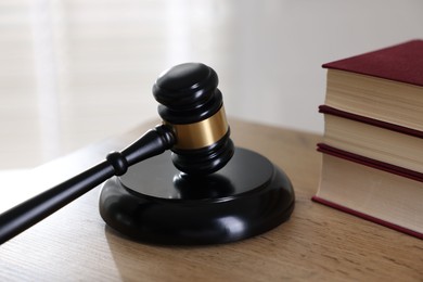 Photo of Judge's gavel and books on wooden table indoors, closeup