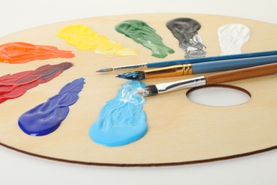 Photo of Wooden palette with paints and brushes on white background, closeup