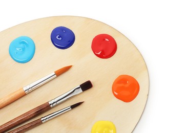 Photo of Wooden palette with paints and brushes isolated on white, top view