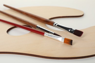 Photo of Wooden palette and brushes on white background, closeup