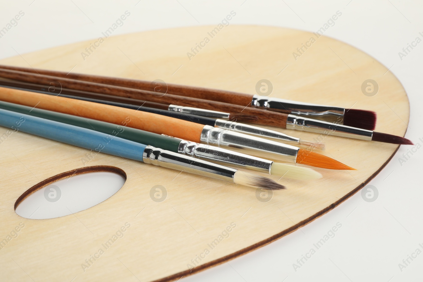 Photo of Wooden palette and brushes on white background, closeup