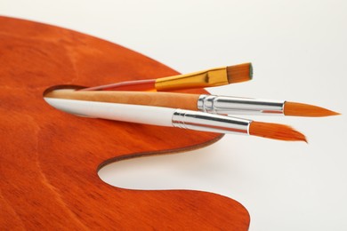 Photo of Wooden palette and brushes on white background, closeup