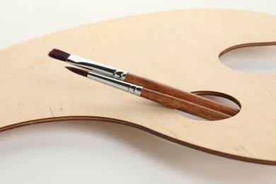 Photo of Wooden palette and brushes on white background, closeup