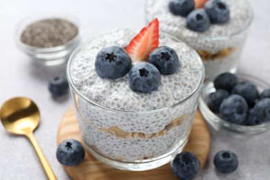 Photo of Delicious pudding with chia seeds, yogurt, blueberries, granola and strawberry on light grey table, closeup. Superfood
